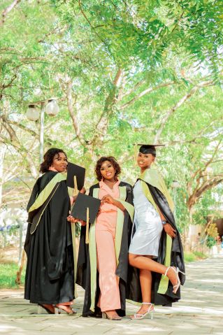 Three happy graduates celebrate their achievement outdoors in cap and gown.